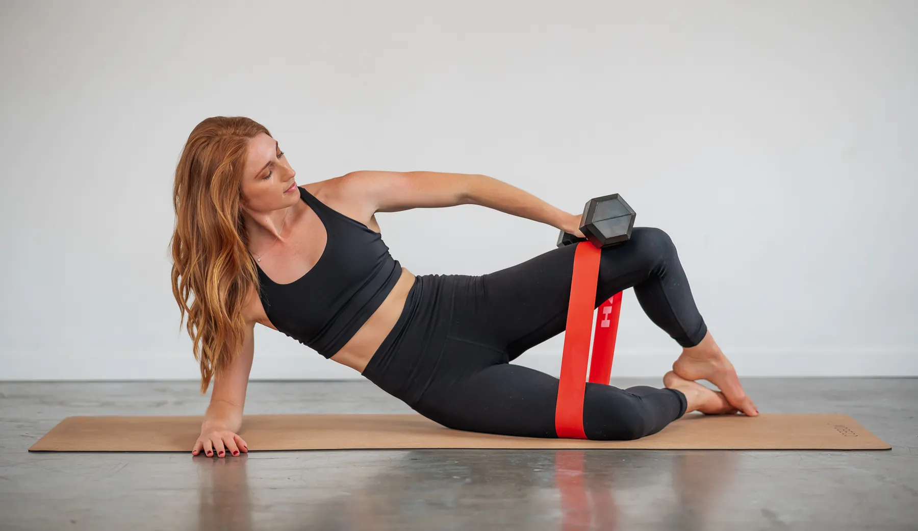 Bridget doing a side-lying Pilates exercise with a resistance band and dumbbell